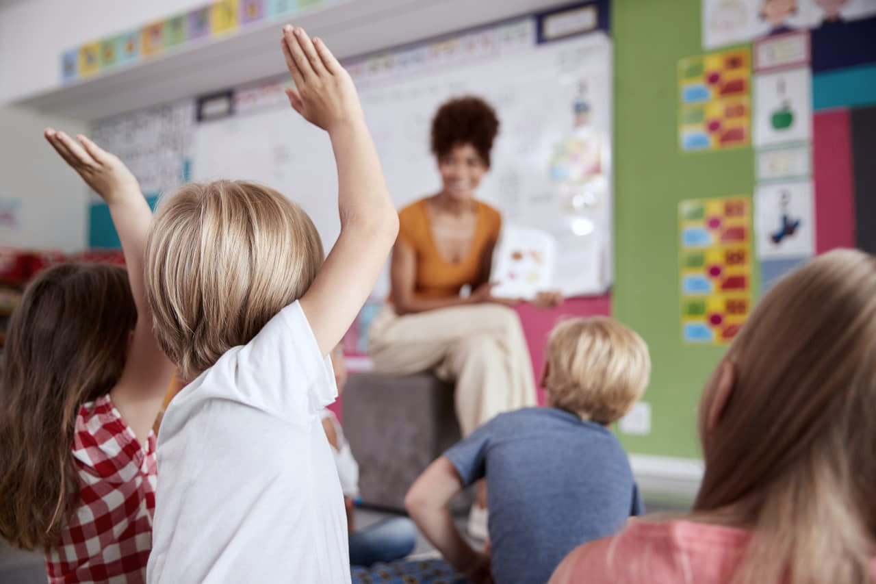 Crianças com as mãos levantadas durante a aula do ministério infantil, com a professora conduzindo a lição
