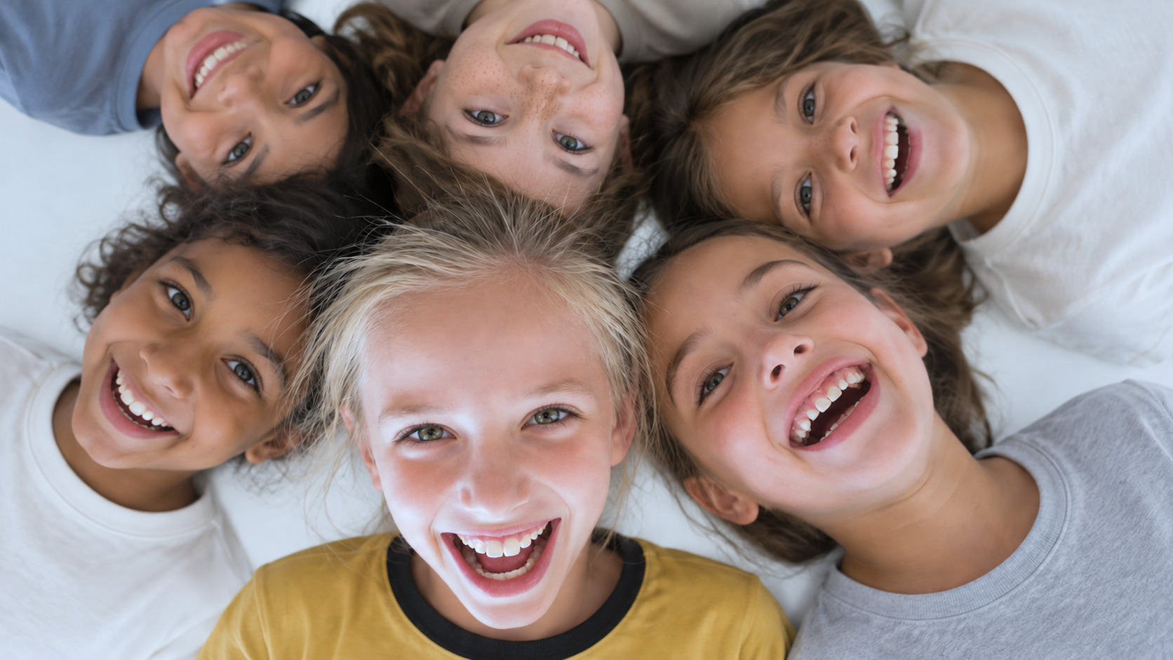 Seis crianças deitadas em roda, sorrindo e olhando para cima, durante o culto infantil